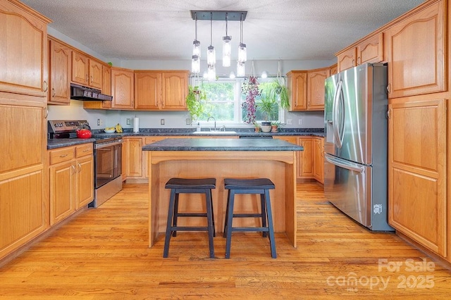 kitchen with a breakfast bar area, under cabinet range hood, a center island, dark countertops, and appliances with stainless steel finishes