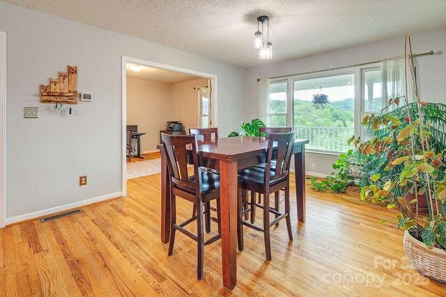 dining room with light wood-type flooring, visible vents, baseboards, and a textured ceiling
