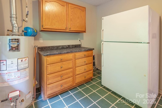 kitchen featuring freestanding refrigerator, water heater, dark tile patterned floors, and dark countertops
