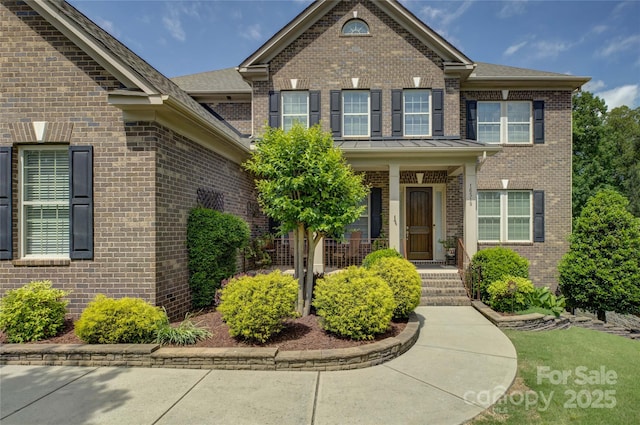 traditional home featuring covered porch, brick siding, and a standing seam roof