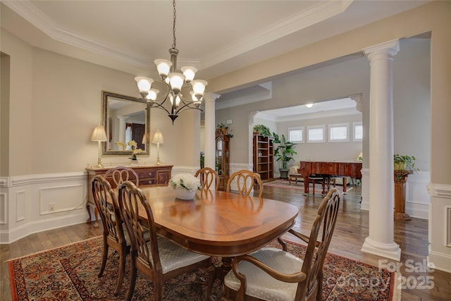dining area featuring crown molding, decorative columns, a wainscoted wall, and hardwood / wood-style floors