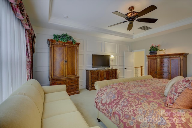 bedroom with visible vents, ornamental molding, light carpet, a tray ceiling, and a ceiling fan
