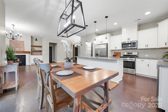 dining room featuring a chandelier, a glass covered fireplace, dark wood finished floors, recessed lighting, and visible vents