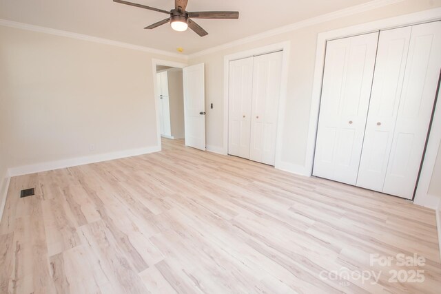 451 S Strand Dr, Norwood, NC 28128 - unfurnished bedroom featuring two closets, ornamental molding, visible vents, and light wood-type flooring