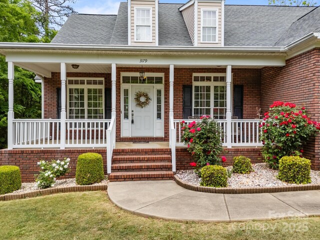 property entrance featuring covered porch, brick siding, and a shingled roof