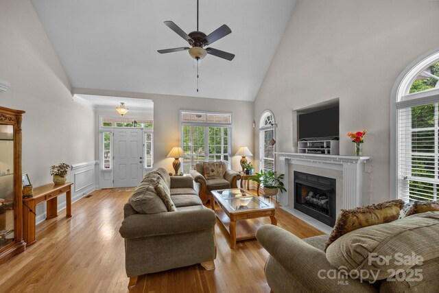 living room featuring a fireplace with flush hearth, high vaulted ceiling, ceiling fan, and light wood-type flooring