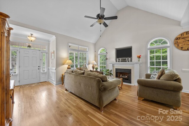 living room with a ceiling fan, a fireplace, high vaulted ceiling, baseboards, and light wood-style floors