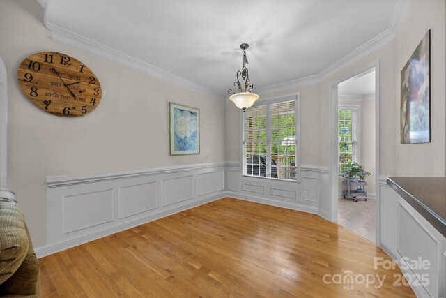 unfurnished dining area with wainscoting, ornamental molding, and light wood-type flooring