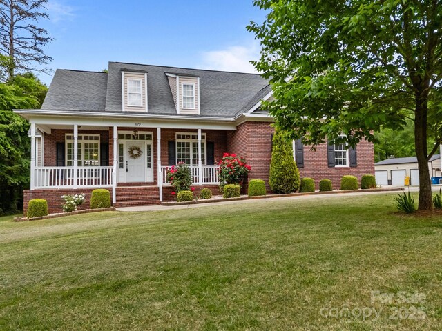 view of front of home with brick siding, a shingled roof, a front lawn, and covered porch