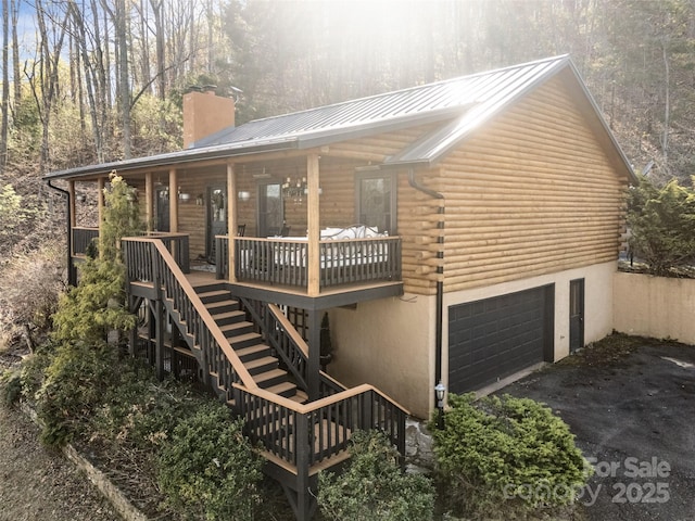 view of property exterior with covered porch, a chimney, log siding, and stairs