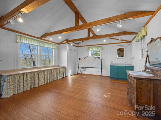 interior space with light wood-style flooring, rail lighting, lofted ceiling with beams, and a sink