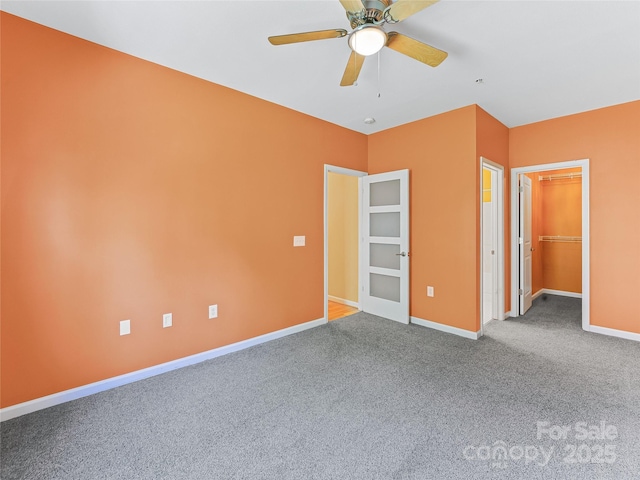 unfurnished bedroom with carpet flooring, baseboards, a spacious closet, a ceiling fan, and a closet