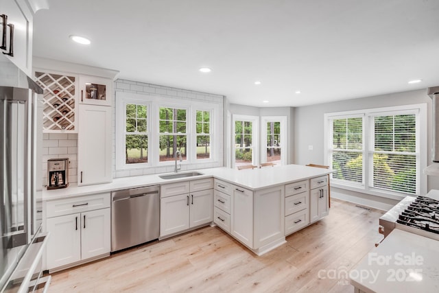 kitchen with white cabinets, stainless steel appliances, light wood-style flooring, and a sink
