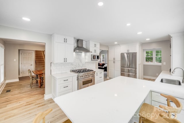 kitchen featuring decorative backsplash, a sink, appliances with stainless steel finishes, light countertops, and wall chimney exhaust hood