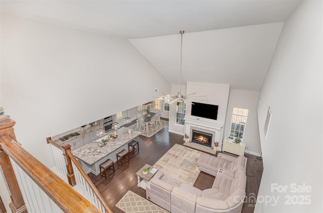 living area with a fireplace, wood finished floors, a ceiling fan, and high vaulted ceiling