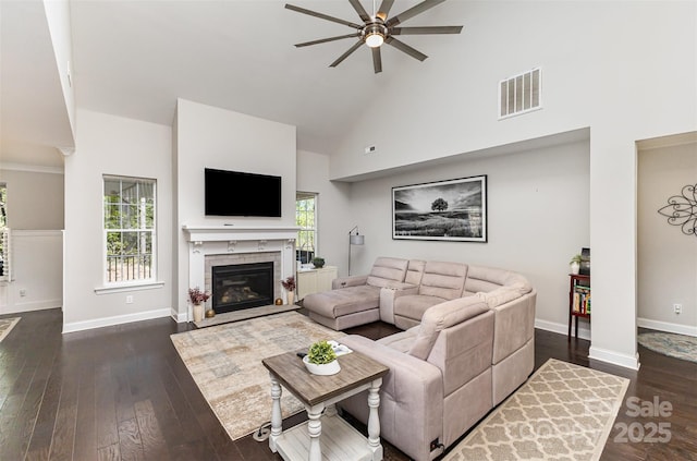 living room with dark wood-type flooring, visible vents, a ceiling fan, and high vaulted ceiling