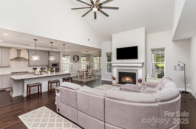 living room with baseboards, recessed lighting, a ceiling fan, high vaulted ceiling, and dark wood-type flooring