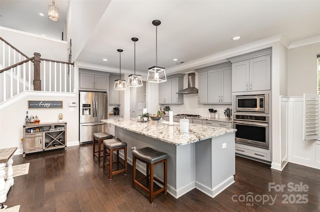 kitchen featuring wall chimney range hood, crown molding, appliances with stainless steel finishes, dark wood-style flooring, and gray cabinetry