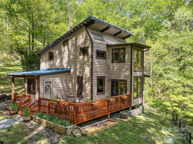 back of property with a view of trees, metal roof, and a deck