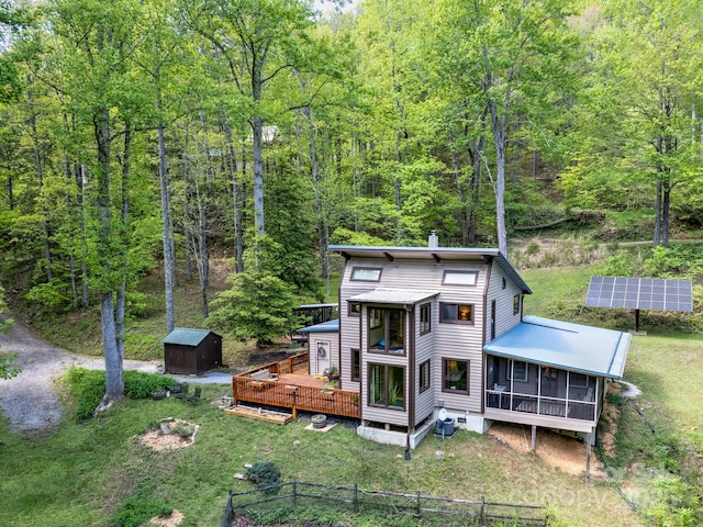 back of house with a forest view, a storage shed, an outbuilding, ground mounted solar panels, and a sunroom