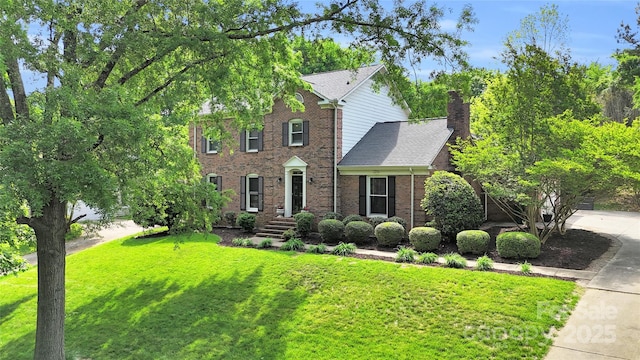 colonial house featuring a chimney, a front lawn, and brick siding