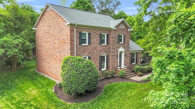 view of front of house with a shingled roof, brick siding, and a front yard
