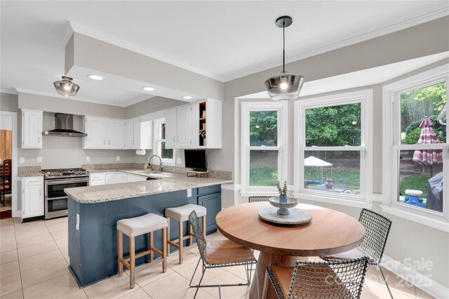 kitchen featuring wall chimney exhaust hood, a peninsula, white cabinetry, range with two ovens, and crown molding