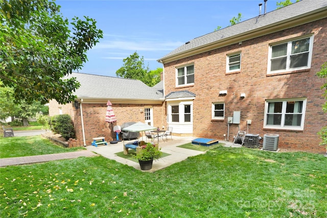 rear view of house with a patio, a lawn, roof with shingles, and central AC unit