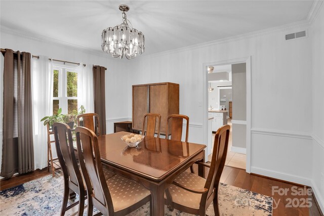 dining space with wood finished floors, visible vents, ornamental molding, and a chandelier