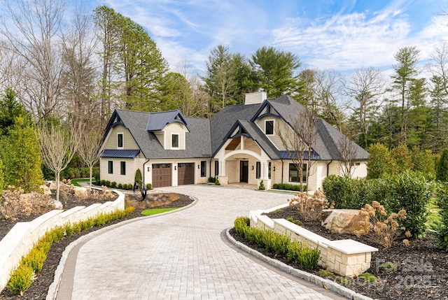 view of front facade with a chimney, curved driveway, and a garage