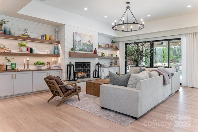 living area with light wood finished floors, an inviting chandelier, a fireplace, and recessed lighting