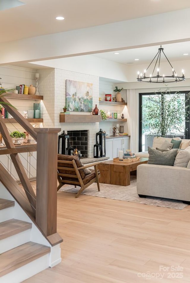 living room featuring recessed lighting, light wood finished floors, a fireplace, stairs, and a notable chandelier
