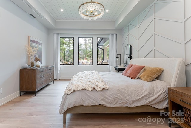 bedroom featuring baseboards, light wood-style floors, a chandelier, and a raised ceiling