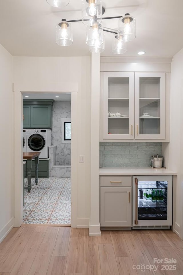 bar featuring light wood finished floors, baseboards, washing machine and dryer, backsplash, and wine cooler