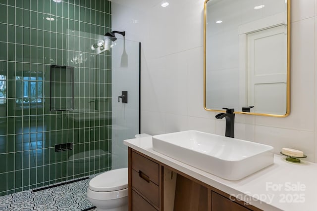 bathroom with tile walls, toilet, vanity, and a tile shower