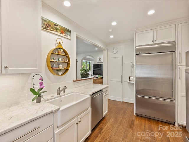 kitchen featuring stainless steel appliances, wood finished floors, a sink, light stone countertops, and white cabinetry