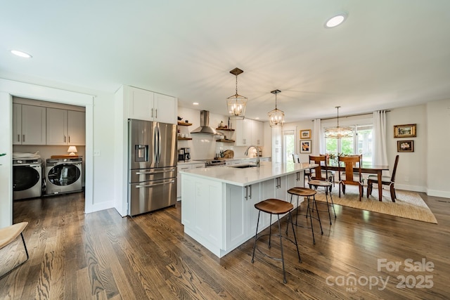kitchen with stainless steel appliances, washing machine and dryer, a kitchen bar, wall chimney range hood, and open shelves