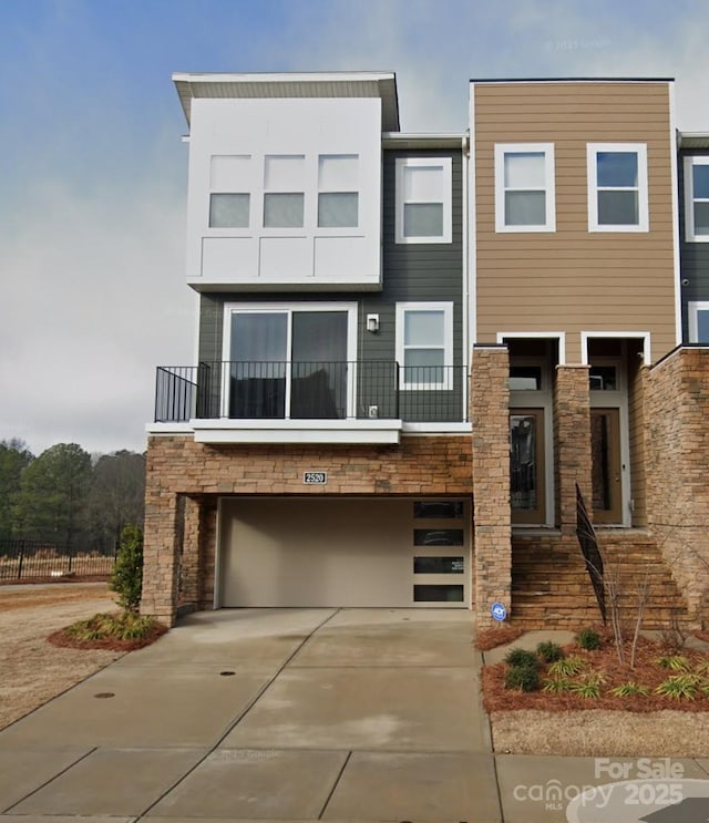view of front of property with stone siding, an attached garage, a balcony, and concrete driveway