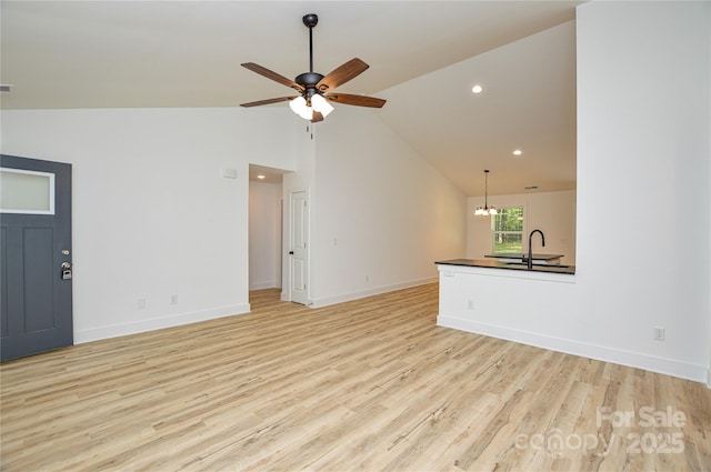 unfurnished living room featuring lofted ceiling, baseboards, recessed lighting, light wood-style flooring, and ceiling fan with notable chandelier