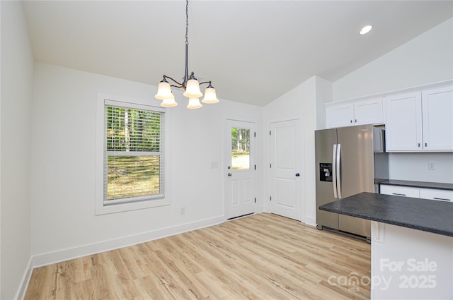 kitchen with dark countertops, vaulted ceiling, a notable chandelier, stainless steel fridge, and white cabinetry