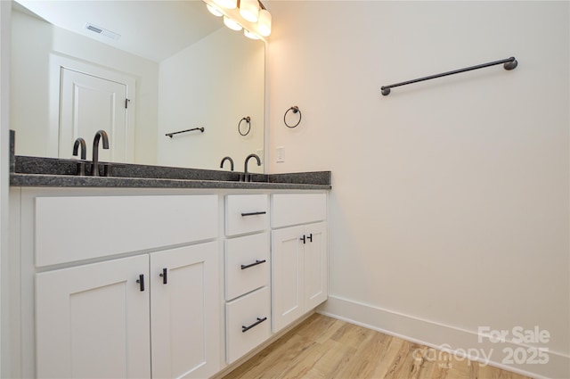 full bath featuring double vanity, visible vents, wood finished floors, a sink, and baseboards