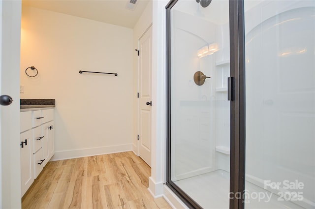 bathroom with vanity, baseboards, wood finished floors, and a stall shower