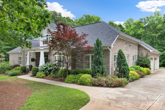 view of side of home with brick siding, driveway, a shingled roof, and a garage