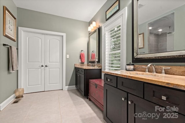 full bath with a sink, a tile shower, baseboards, tile patterned flooring, and two vanities