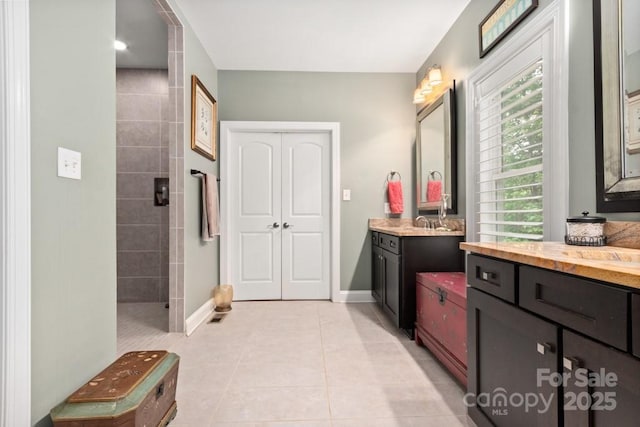 bathroom with a tile shower, baseboards, vanity, and tile patterned floors
