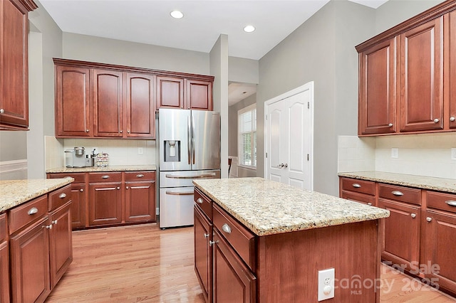 1105 Hoyle Ln, Waxhaw, NC 28173 - kitchen with light wood-type flooring, a kitchen island, light stone countertops, decorative backsplash, and stainless steel fridge