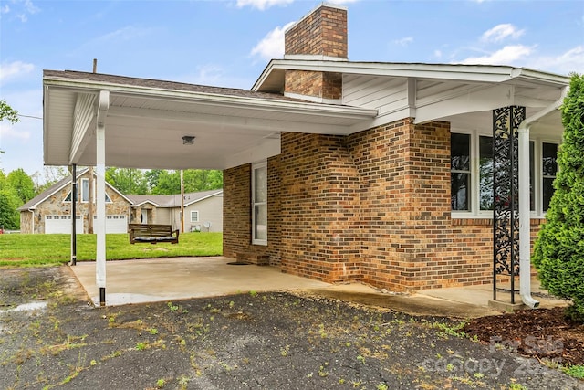 exterior space featuring a carport, a lawn, a chimney, and brick siding