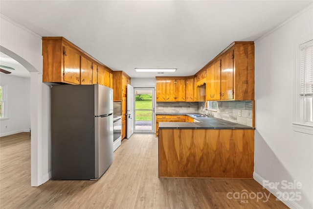 kitchen featuring brown cabinets, a healthy amount of sunlight, a sink, freestanding refrigerator, and a peninsula