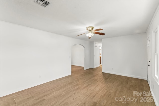 spare room featuring a ceiling fan, wood finished floors, arched walkways, baseboards, and visible vents