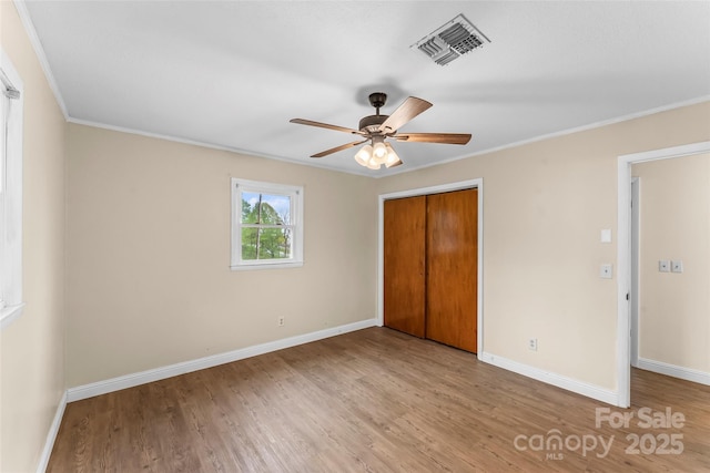 unfurnished bedroom featuring wood finished floors, visible vents, a closet, and crown molding